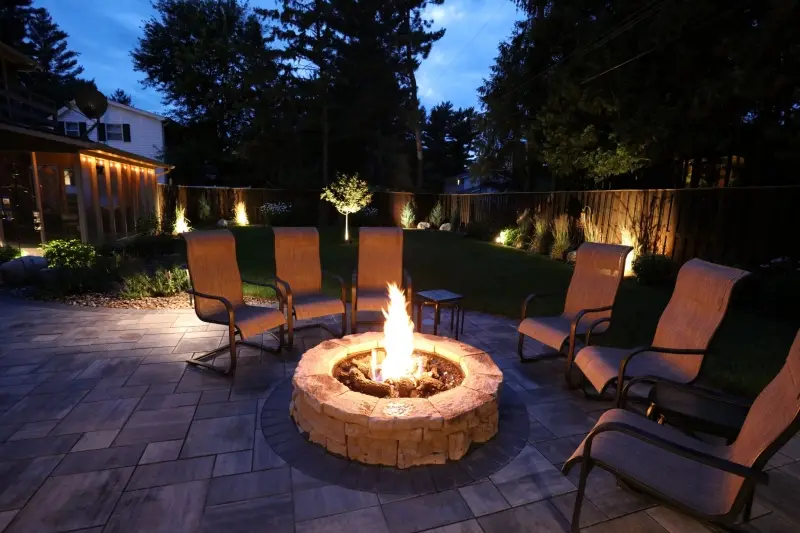 Garden patio at night with landscape lighting and a fire feature